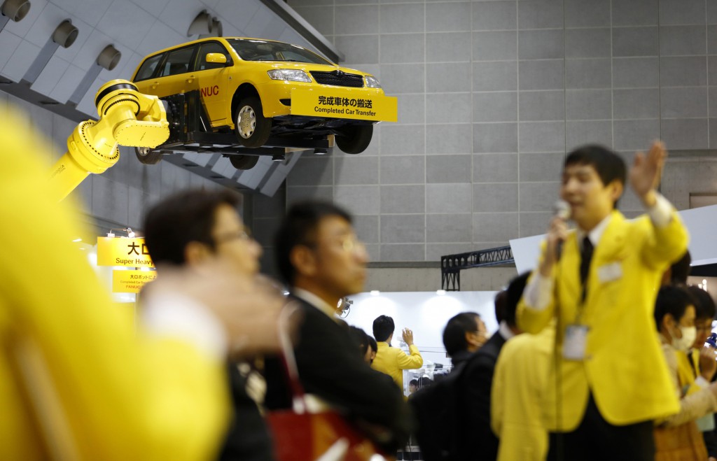 A Fanuc Corp. employee speaks to attendees as an industrial robots moves a vehicle during a demonstration at the International Robot Exhibition 2015 in Tokyo, Japan, on Tuesday, Dec. 2, 2015. Photographer: Tomohiro Ohsumi/Bloomberg